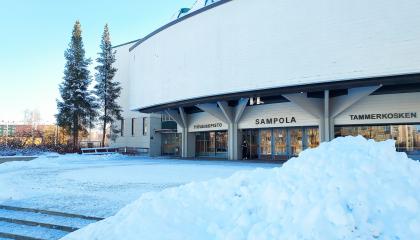 The Sampola building. There are conifer trees next to it, and snowdrifts in the foreground.