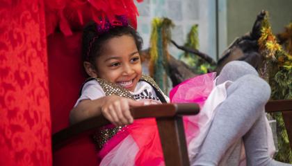 Lapsi istuu punaisessa nojatuolissa roolivaatteet päällä ja nauraa.