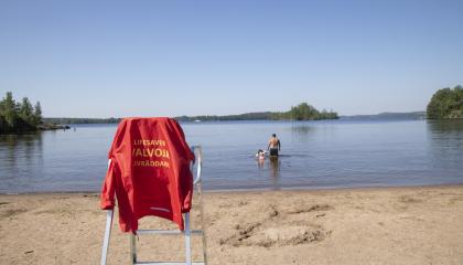 Pyynikin uimarannalla uimavalvojan tuoli ja takki, vedessä ihmisiä uimassa.