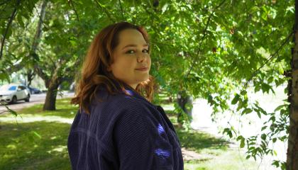 Nuori punatukkainen nainen seisoo vihreässä maisemassa ja hymyilee. 