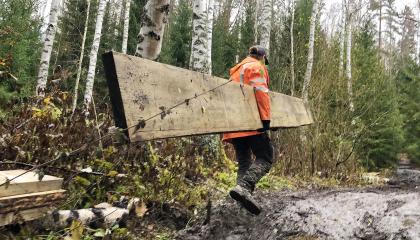 Henkilö kantaa pitkospuuta mutaisella polulla.