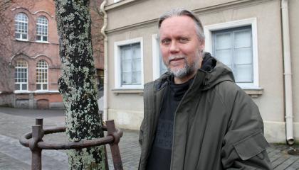 Mies seisoo puun vieressä takki päällä.