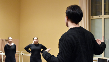 Henkilö seisoo salissa. Taka-alalla kaksi henkilöä kuuntelee ohjeistusta.