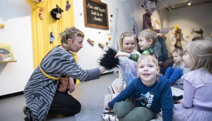 Ohjaaja leikittää lattialla istuvaa lasten ryhmää