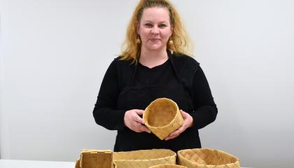 Henkilö pitelee tuohitöitä käsissään. Etualalla koreja.