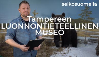 Mies pitää kädessään kirjoitusalustaa. Taustalla kuva suomaisemasta, jossa mänty ja karhu.