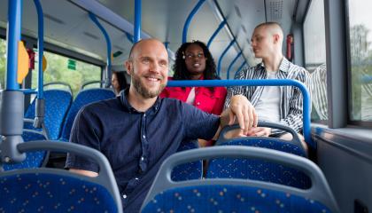 Mies istuu hymyillen bussin kyydissä.