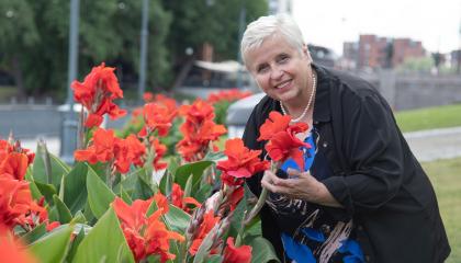 Henkilö seisoo kukkien vieressä ja katsoo kameraan.