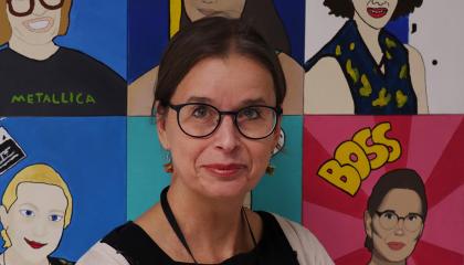 Rehtori Tuija Ylöniemi kuvattuna itseään esittävien maalattujen kuvien koostetaulun edessä.