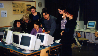 Seitsemän henkilöä seisoo tietokoneiden ympärillä luokkaympäristössä.