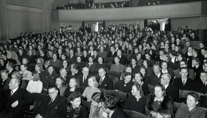 Henkilöistä suuressa luentosalissa, jonka takana on parvi.