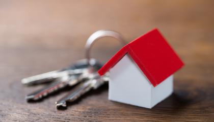 Pöydällä on pienoiskokoinen punakattoinen mökki, jonka vieressä on avainnippu.