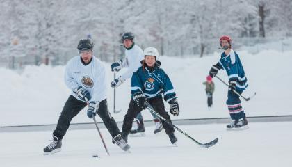 Neljä henkilöä pelaamassa jääkiekkoa luonnonjäällä.