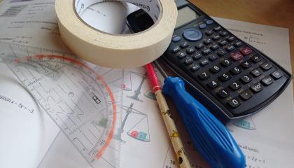 Matematiikan kirjan päällä laskin, maalarinteippiä, ruuvimeisseli, kynä ja piirtokolmio.