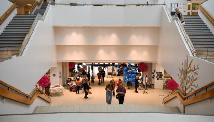 Sampolan aula, jossa henkilöt kävelevät portaita ylös. Aulan reunoilla on ilmapalloja.