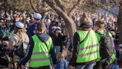 Kolme vihreäliivistä henkilöä kulkee juhlijoiden joukossa ulkona.