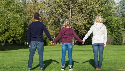 Vanhemmat ja nuori kulkevat käsi kädessä poispäin katsojasta.