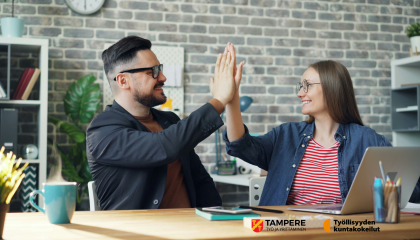 Vanhempi työntekijä ja nuori hymyilevät ja paiskaavat kättä läppärin äärellä.