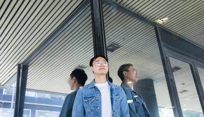 Henkilö kuvattuna niin, että hän heijastuu lasisesta seinästä kolmena.