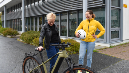 Kaksi henkilöä seisoo pyörän ympärillä pihassa.