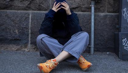 Nuori istuu maassa ja pitelee päätään käsissään.