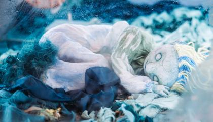 Valkean värinen nukketeatterinukke makoilee sinisen kankaan päällä.