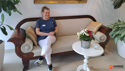 Henkilö istuu biedermeier-sohvalla ja etualalla on pyöreä pöytä, jonka päällä on kukkaruukku.