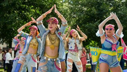 Värikkäästi pukeutuneita naisia tanssimassa kädet ylhäällä pään päällä.