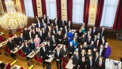 Valtuutetut seisovat raatihuoneen juhlasalissa ja katsovat ylöspäin kameraan.