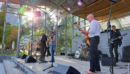 Keski-ikäisten miesten jazz-bändi esiintyy ulkoilmalavalla aurinkoisessa säässä.