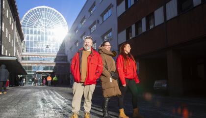 Kolme henkilöä kävelee aurinkoisena talvipäivänä Tullin alueella. Kahdella on päällään punainen ja yhdellä ruskea takki.