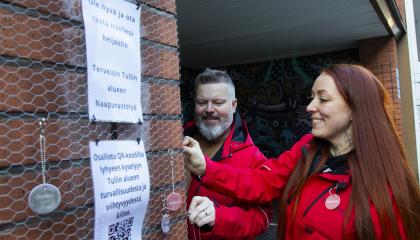 Tullintorin naapurustotyön punatakkiset työntekijät kiinnittävät Tullintorin ulkoseinään hankkeesta kertovaa heijastinta.