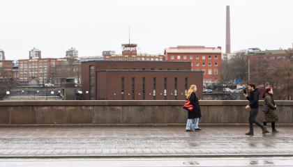 Kolme henkilöä kävelemässä vastakkaisiin suuntiin Hämeensillalla, taustalla Tammerkosken putous ja voimalaitos.
