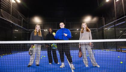 Neljä henkilöä seisoo padelkentällä verkon takana.