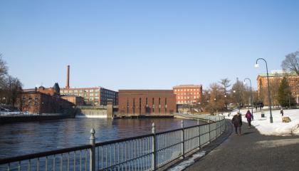 Tammerkosken rannan tuntumassa Koskipuistossa menee kävelytie ja taustalla näkyy voimalaitoksen punatiilisiä rakennuksia.