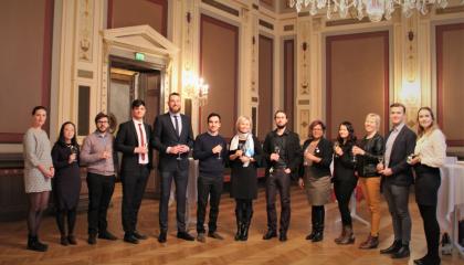 a group of people standing in a row in a stylish environment with wine glasses in their hands.