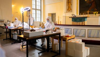 Valkoisiin haalareihin pukeutuneet tutkijat tutkivat valojen alla pääkalloja.