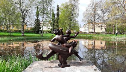 Kahta kaloilla ratsastavaa poikaa esittävä veistos lammen rannalla.
