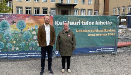Jaani Haapasalo ja Annamaija Saarela seisovat ulkovaatteissa Nekalan kulttuurikeskuksen työmaan edessä. Taustalla lakana, jossa lukee "Kulttuuri tulee lähelle".