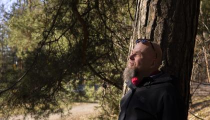 Henkilö nojaa vanhan puun runkoon, jonka oksat täyttävät kuvan taka-alan.