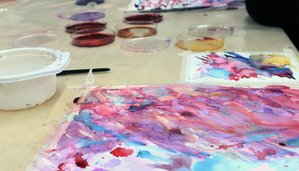 Kuvataidetyö ja luonnonväripurkkeja pöydällä.