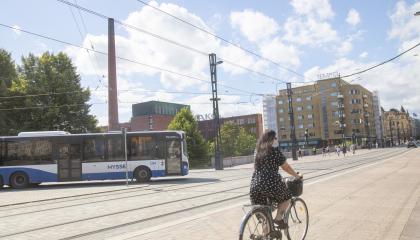 Bussi kääntymässä Hämeenkadulle ja pyöräilijä etualalla, taivaalla kesäpilviä.