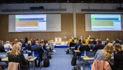 Ihmisiä takaa istumassa, edessä esitys ja henkilöitä.