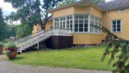 Keltainen kartanorakennus, jonka takana lasierkkeri.