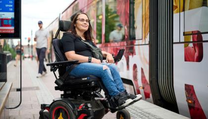 Pyörätuolissa istuva henkilö odottaa laiturilla pääsyä ratikkaan.