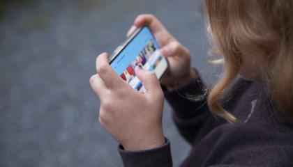 Lapsi pitää puhelinta sormet koukussa ja katsoo ruutua.