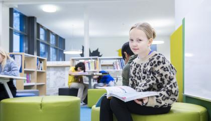 Nuori oppilas istuu kirja sylissä koulun tiloissa.