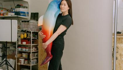 Tummahiuksinen nainen pitää sylissään delfiiniveistosta. 