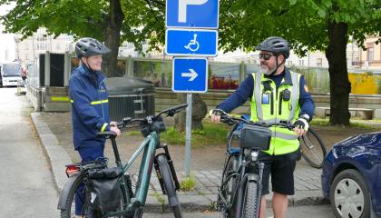 Kaksi henkilöä seisoo pyörien vieressä pysäköintimerkin edessä ja katsovat toisiinsa.