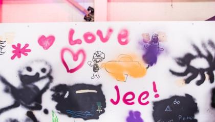 Iloisen näköisiä hahmoja, sydämiä, aurinko ja sanat "Love" ja "Jee" graffitiseinällä.